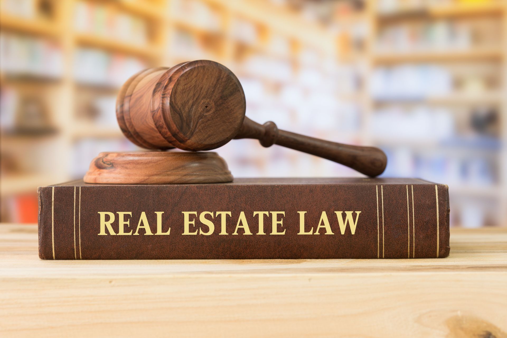 Law book labeled “Real Estate Law” with a gavel on top in a blurred library setting