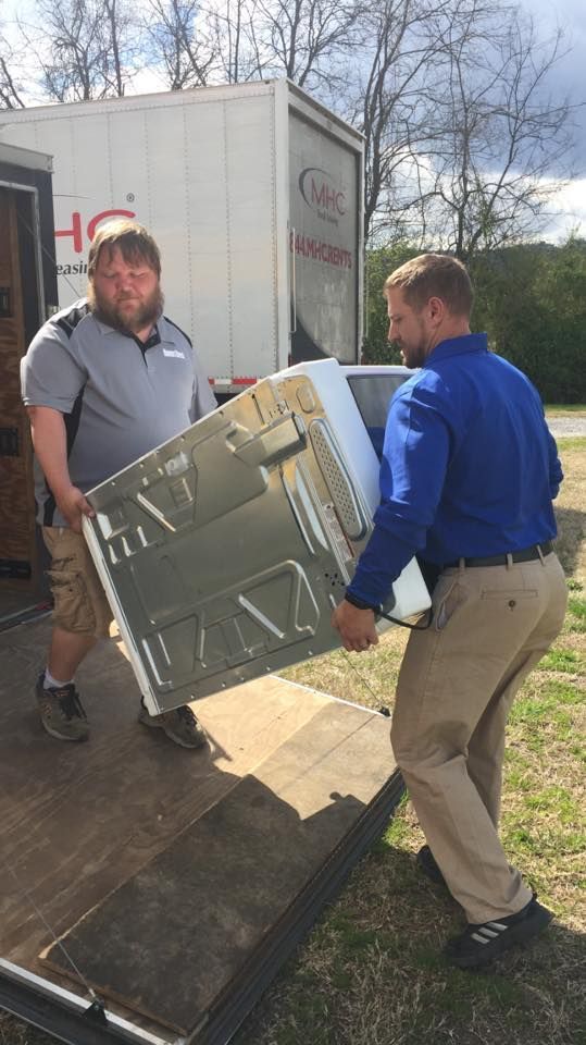 Two men are carrying a refrigerator out of a truck.