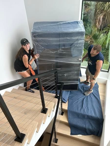 A man and a woman are moving a large item up a set of stairs.