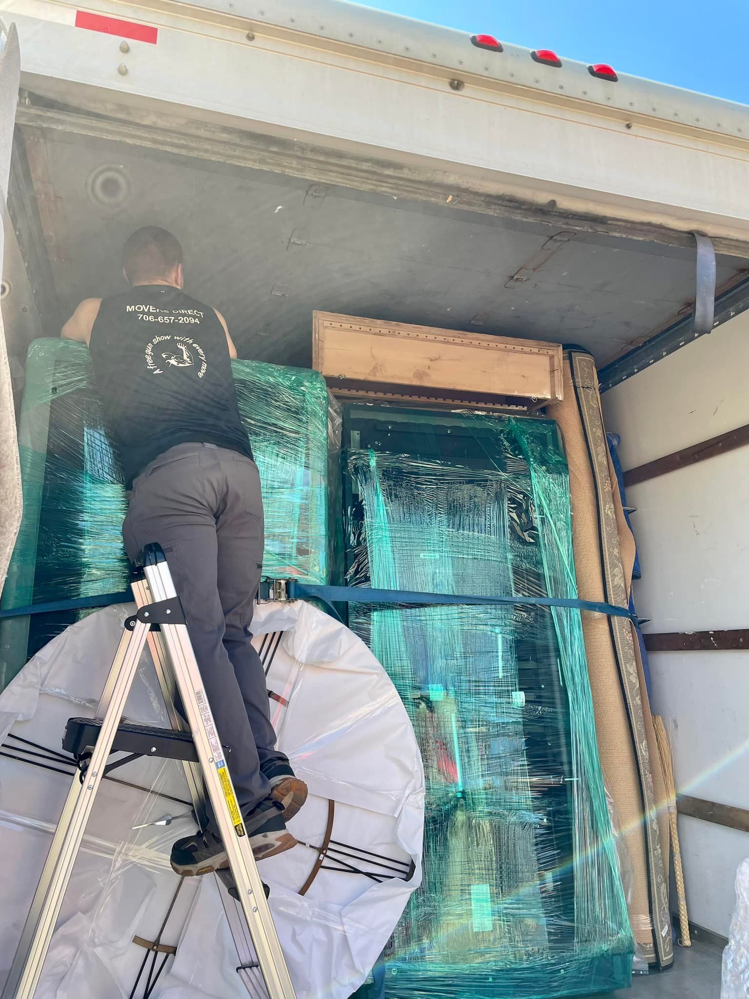 A man is standing on a ladder in the back of a truck.