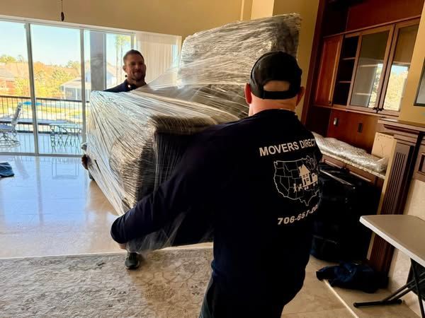 A man is carrying a piano wrapped in plastic in a living room.