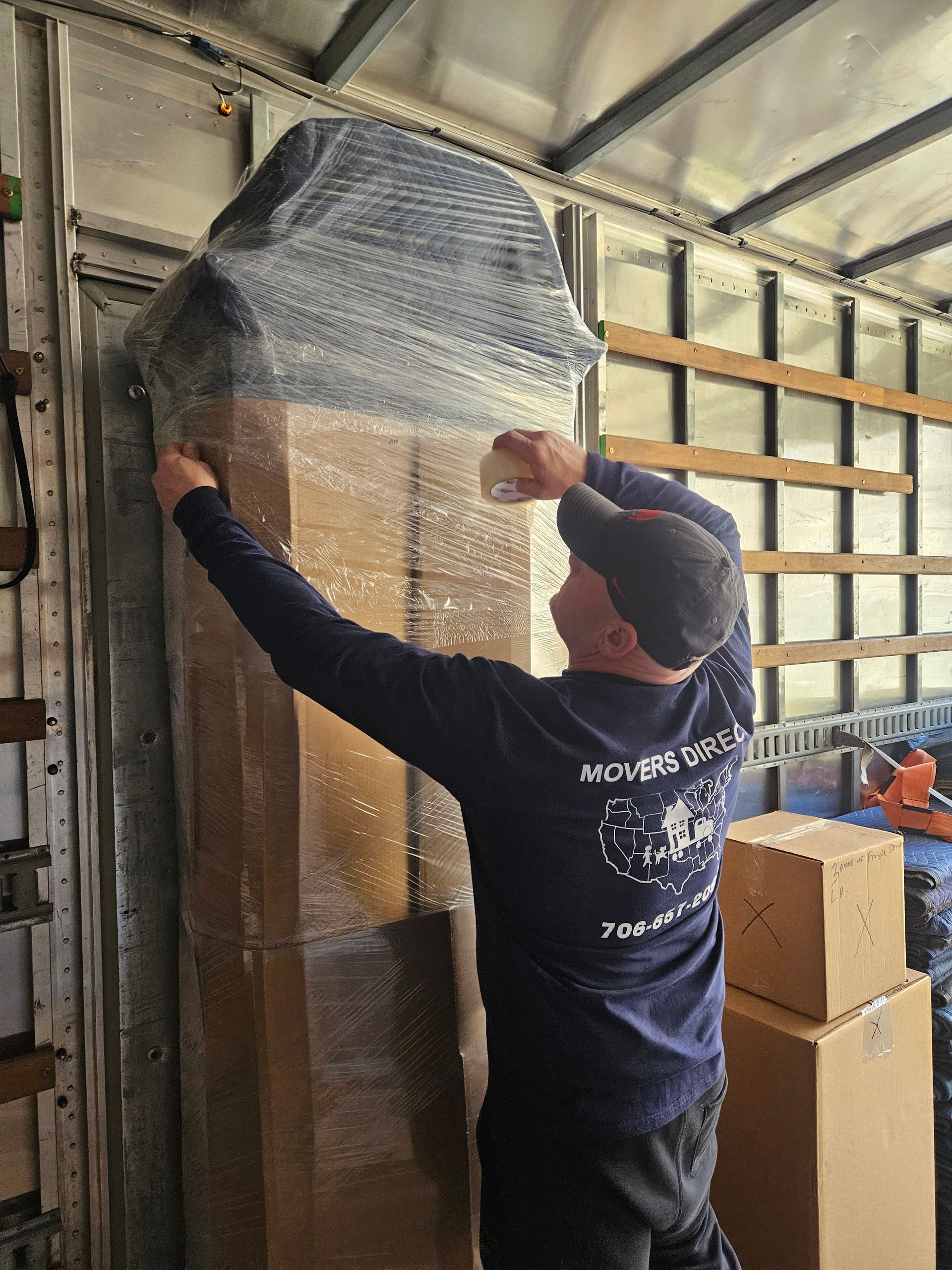 A man is wrapping a large piece of furniture in plastic bubble wrap.