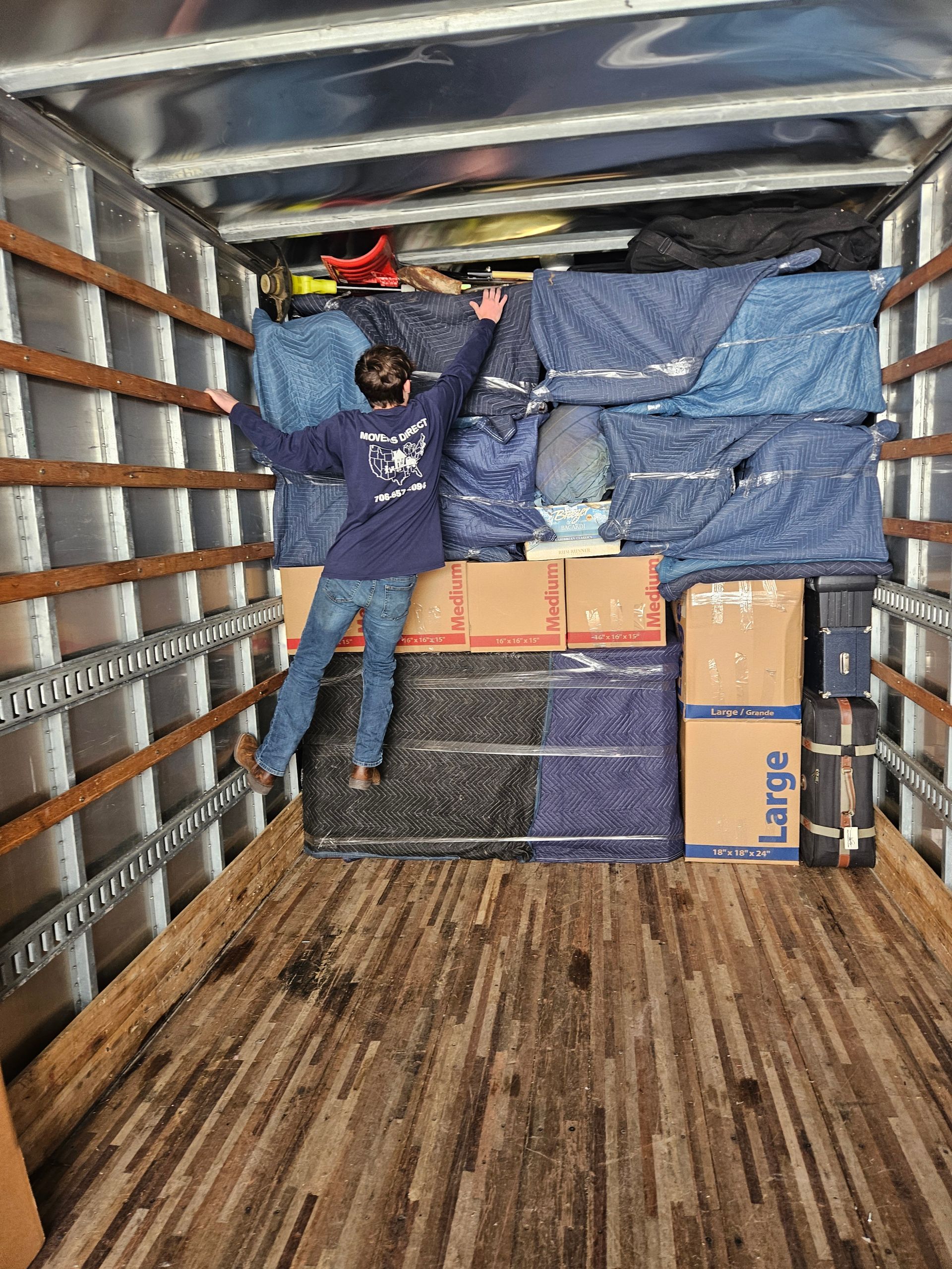 Long view of man reaching for tarp above boxes in a moving van.