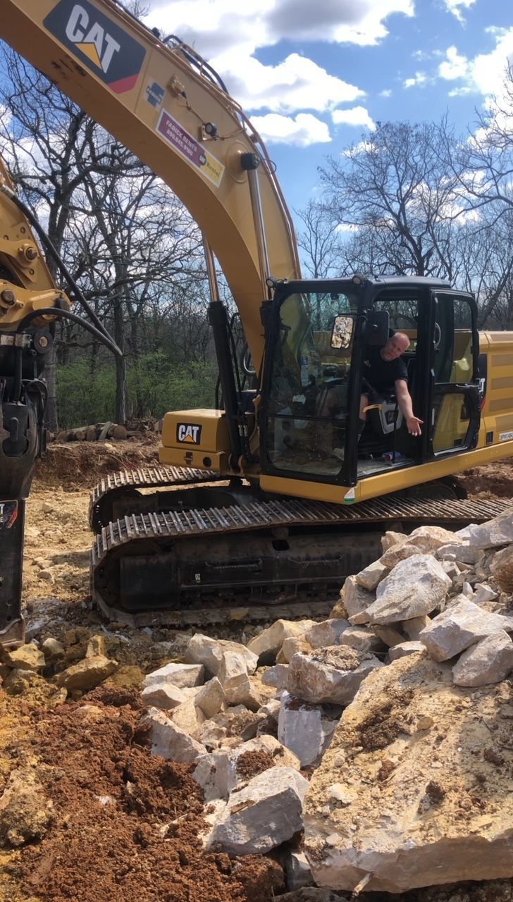 A man is driving a cat excavator in a pile of rocks.
