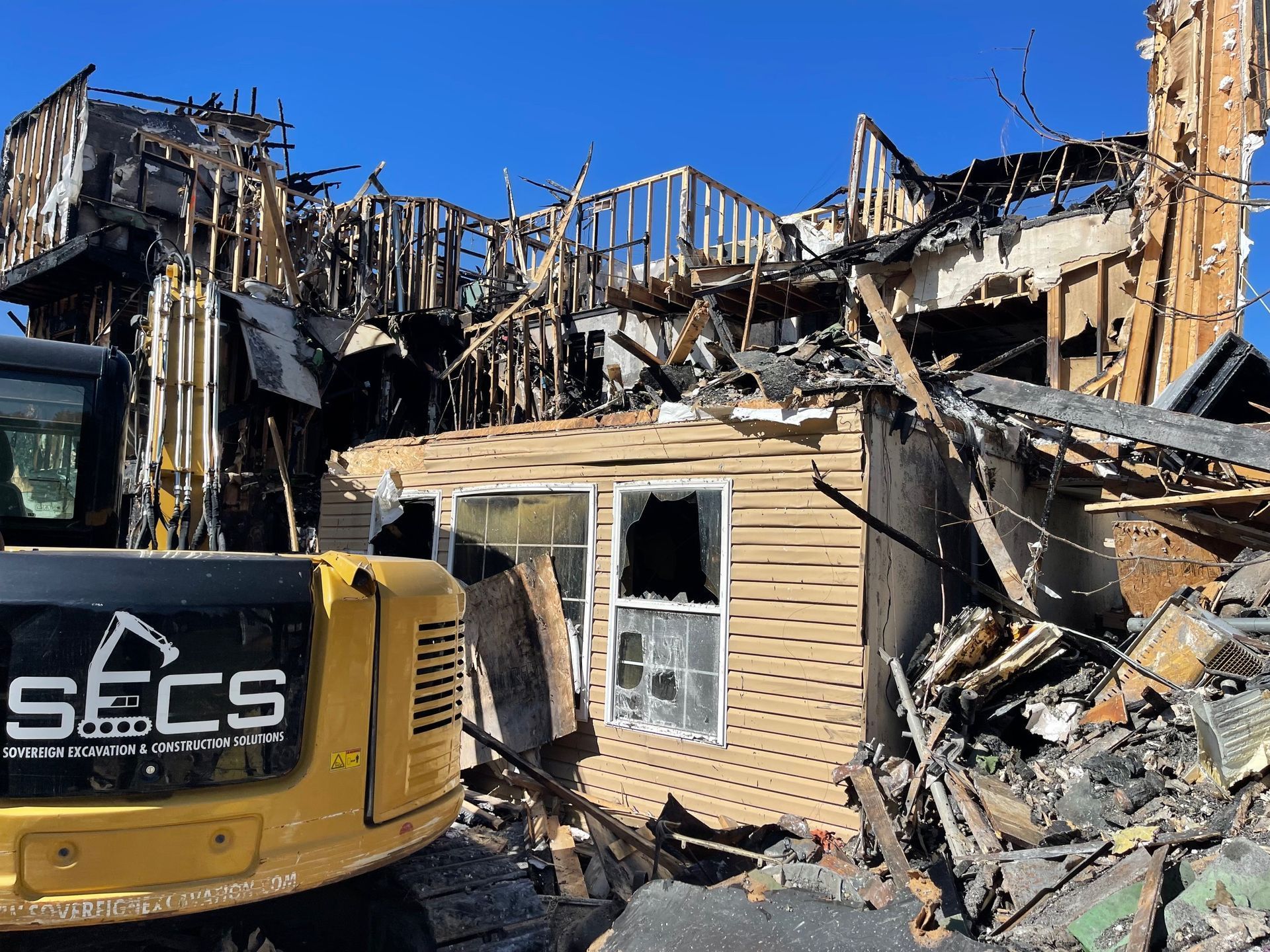 A yellow excavator with secs written on the side is demolishing a house.