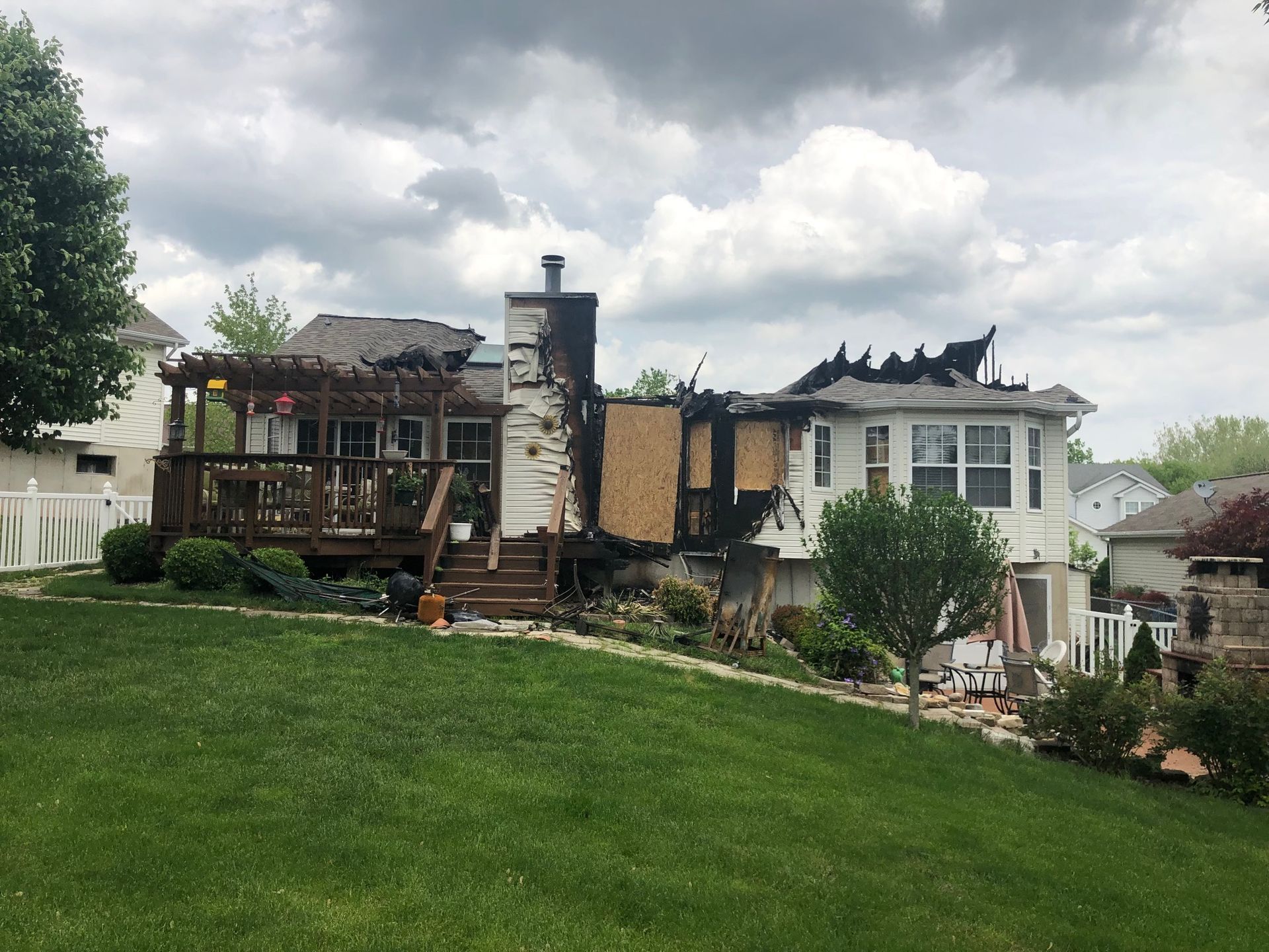 A house that has been damaged by a fire is sitting on top of a lush green hillside.