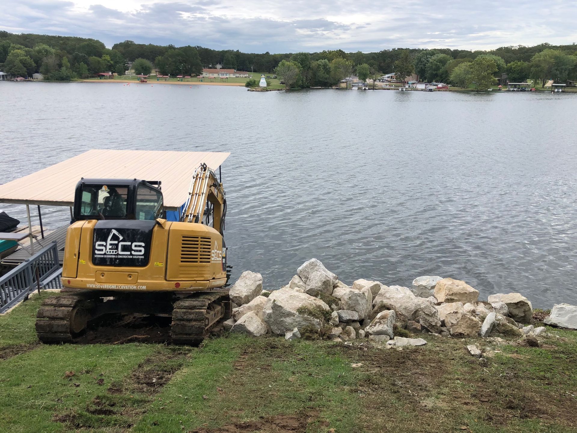 A yellow excavator is working on a dock next to a lake.