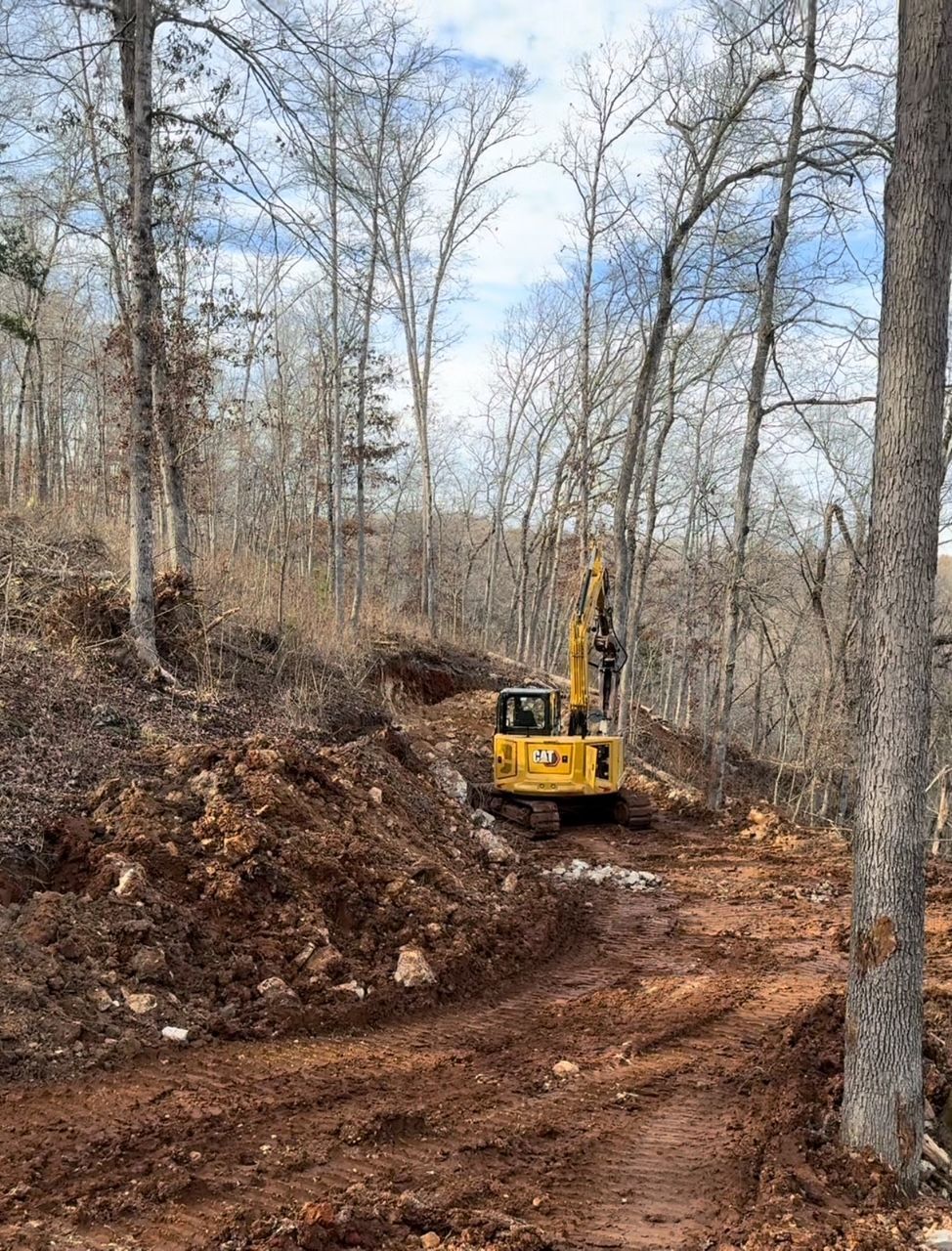 A yellow excavator is driving down a dirt road in the woods.
