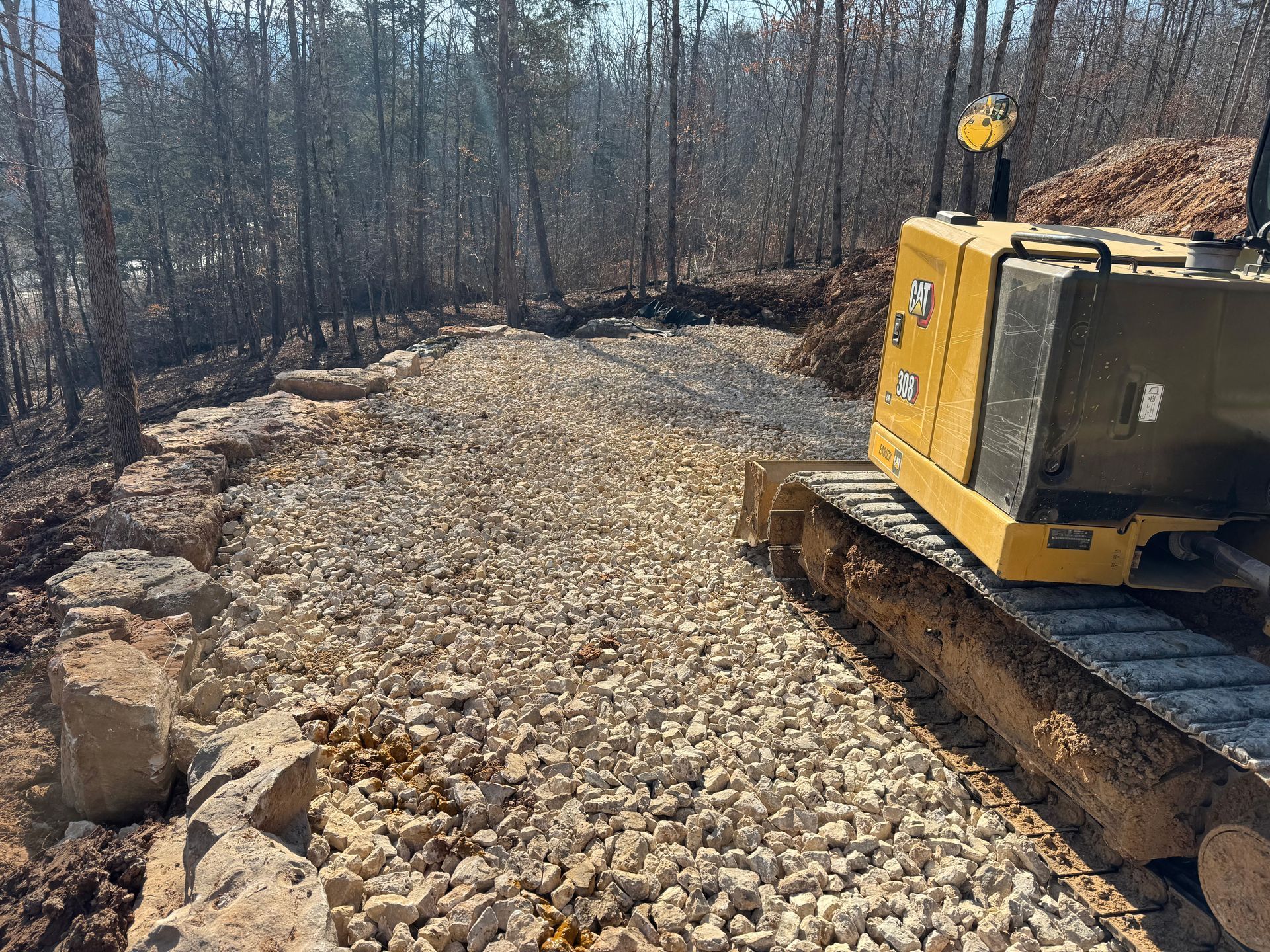 A bulldozer is driving down a dirt road in the woods.