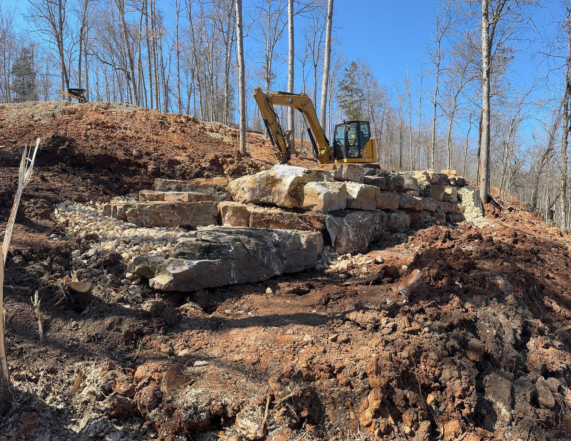 A yellow excavator is sitting on top of a pile of rocks.