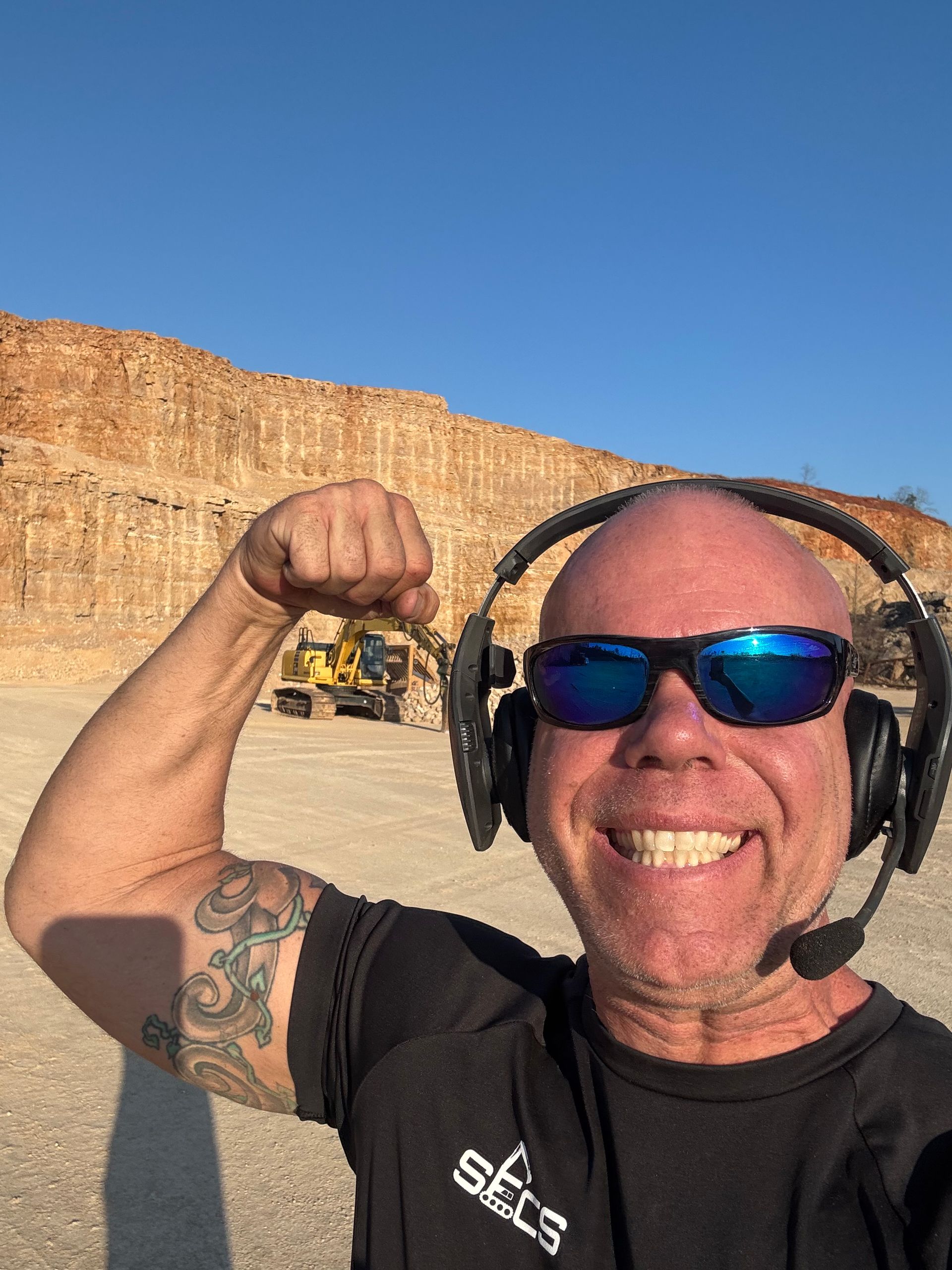 A man wearing headphones and sunglasses is flexing his arm.