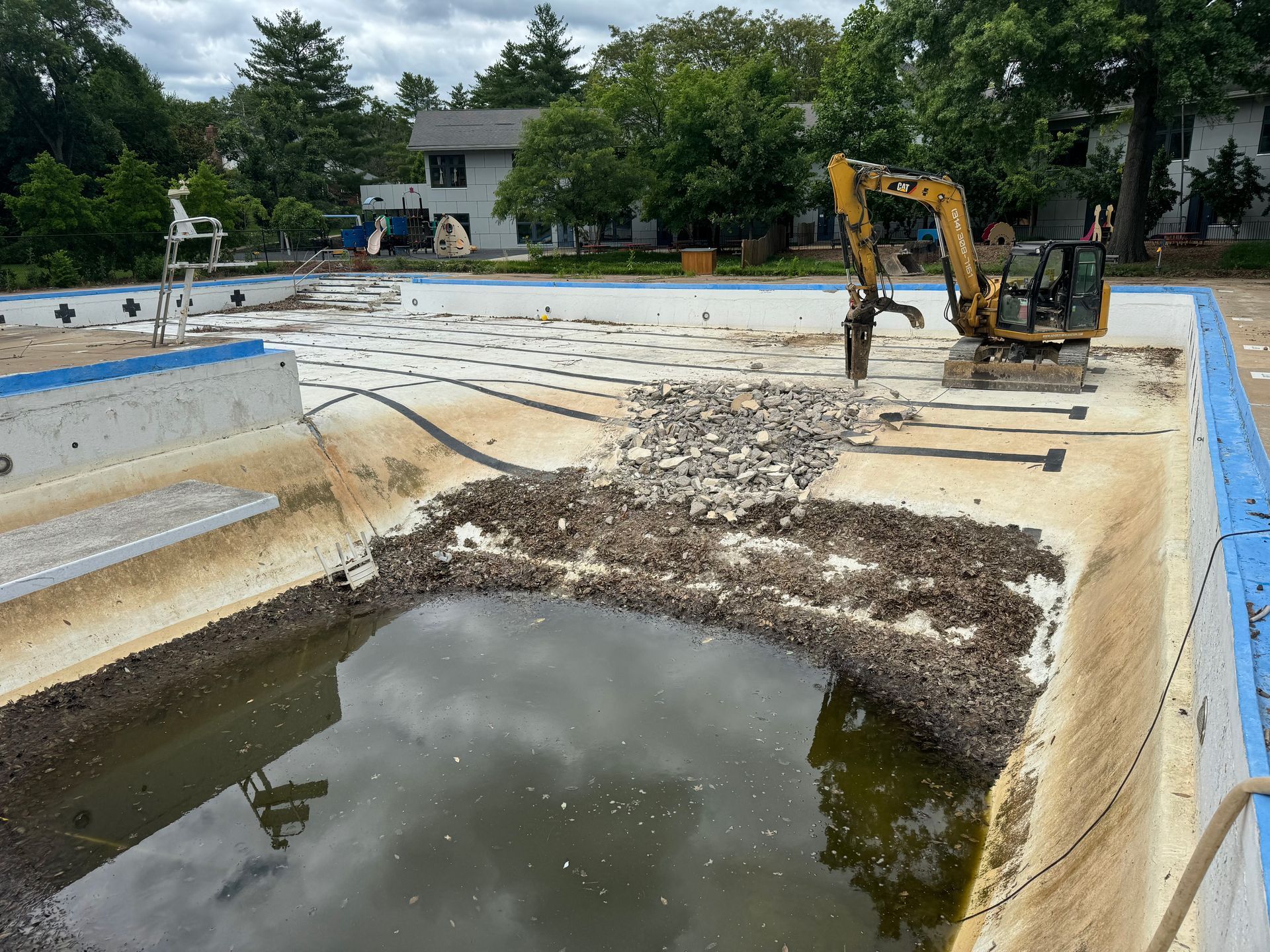 A yellow excavator is working on a swimming pool