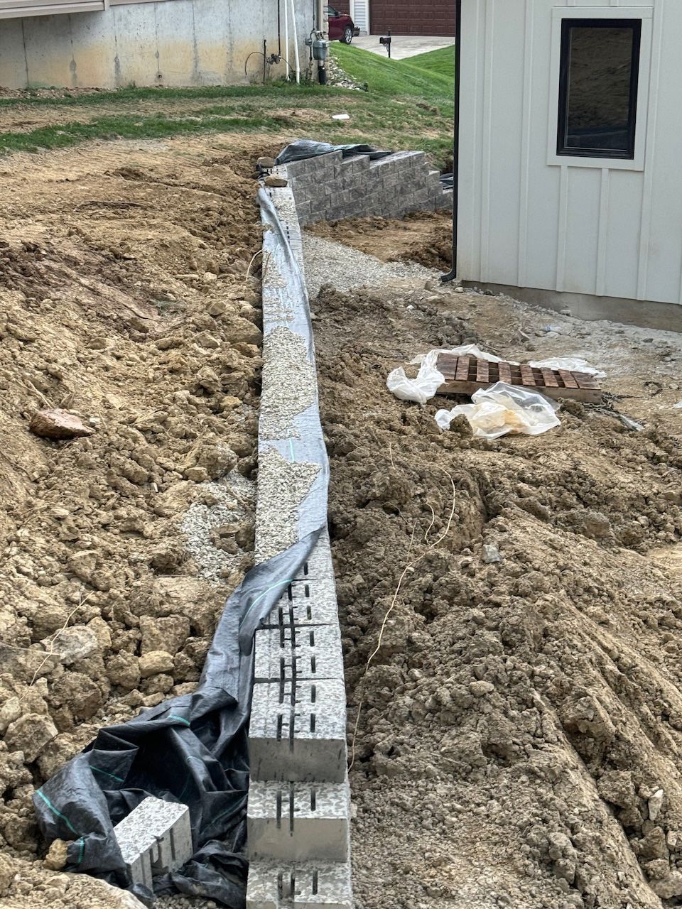 A brick wall is being built in the dirt in front of a house.