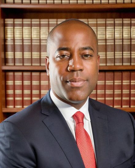 A man in a suit and tie is standing in front of a bookshelf.