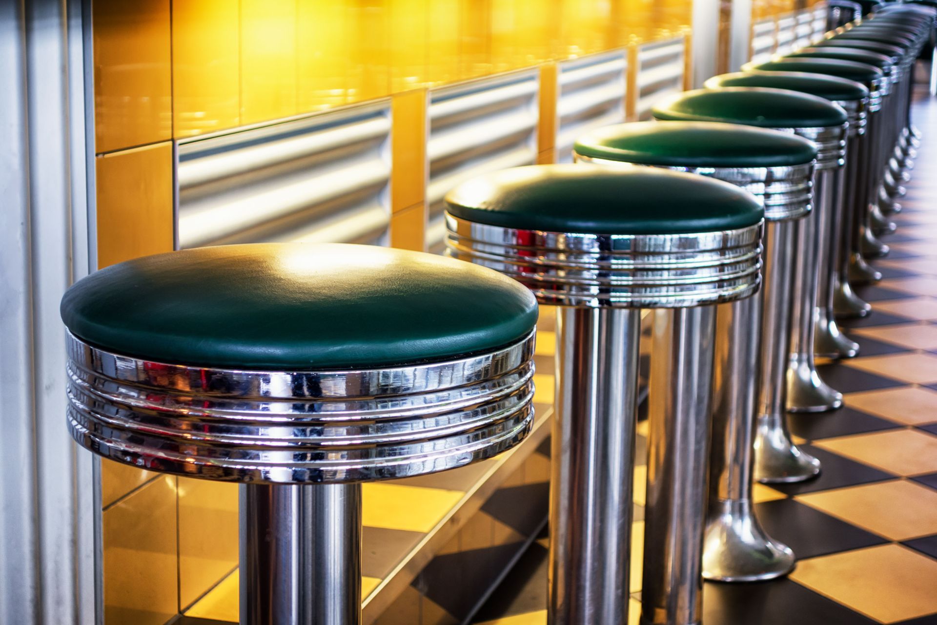 Row of chrome diner stools with green seats along a counter and checkered floor