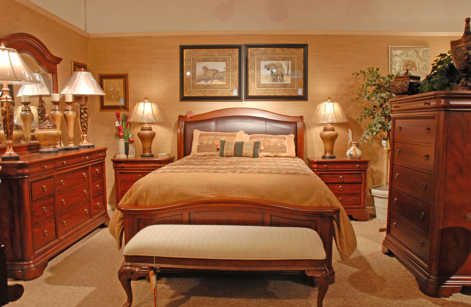 Warm, traditional bedroom with a made bed, wooden dressers, lamps, and framed art on beige walls