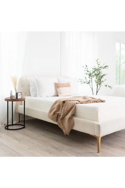 Minimalist white bedroom with low bed, beige throw, black side table, and vase of flowers