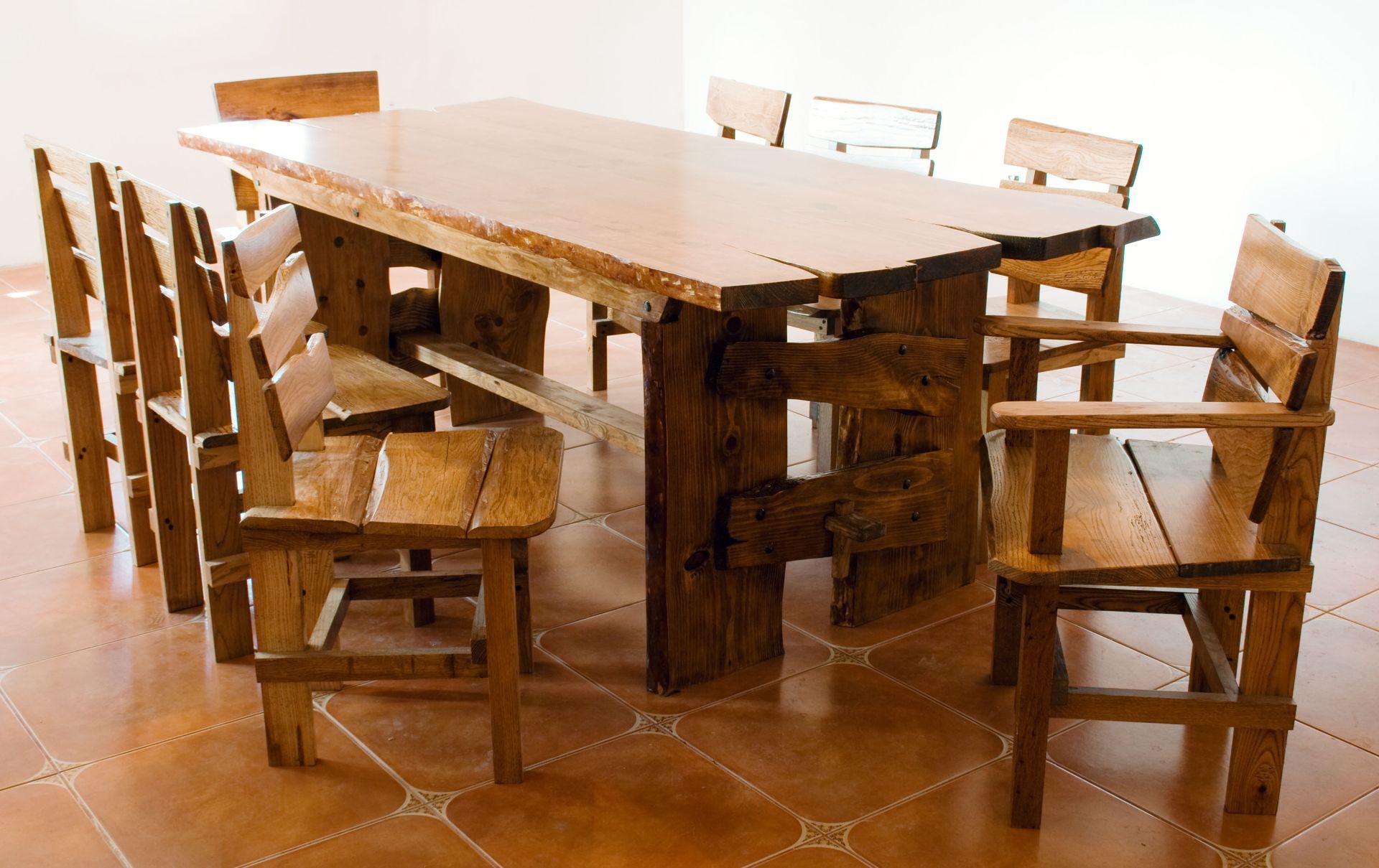 Wooden dining table with several matching chairs on a terracotta tile floor