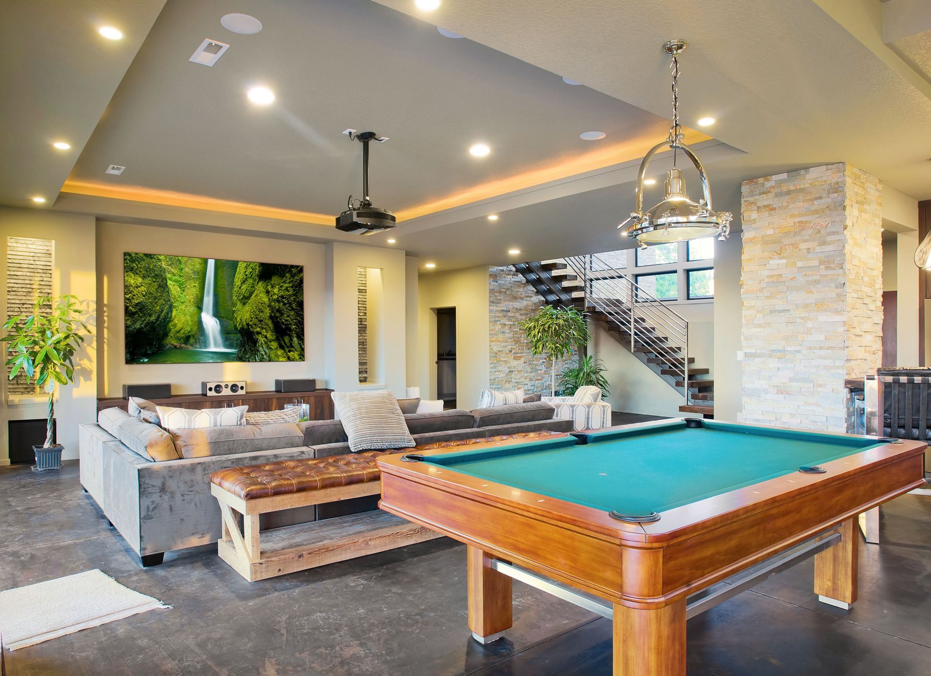 Modern luxury game room with a pool table, sectional sofa, TV, and stone fireplace