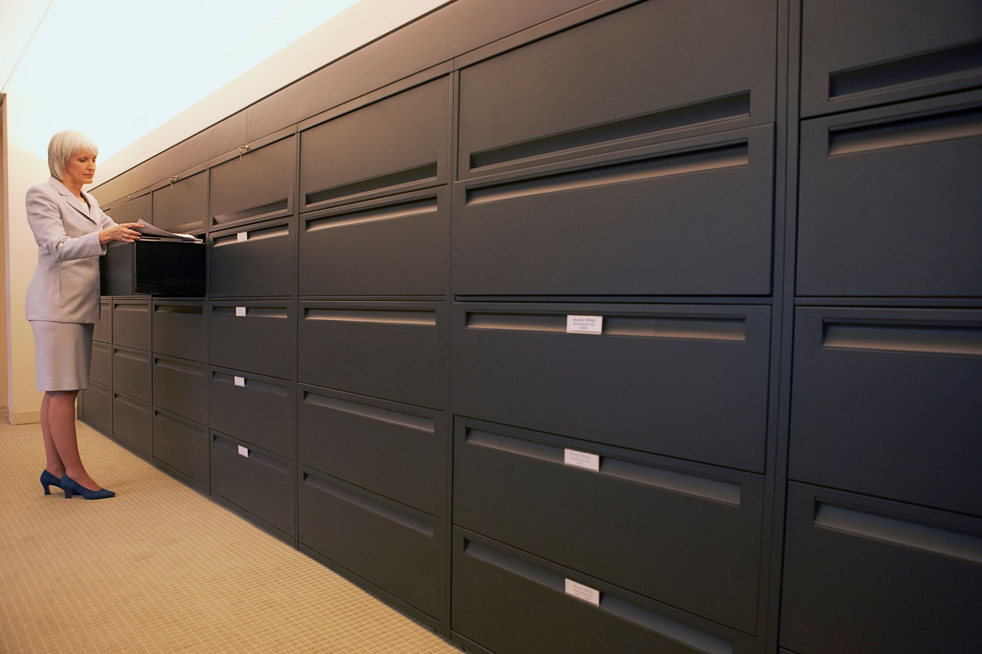 Person using a wall of dark filing cabinets in an office.