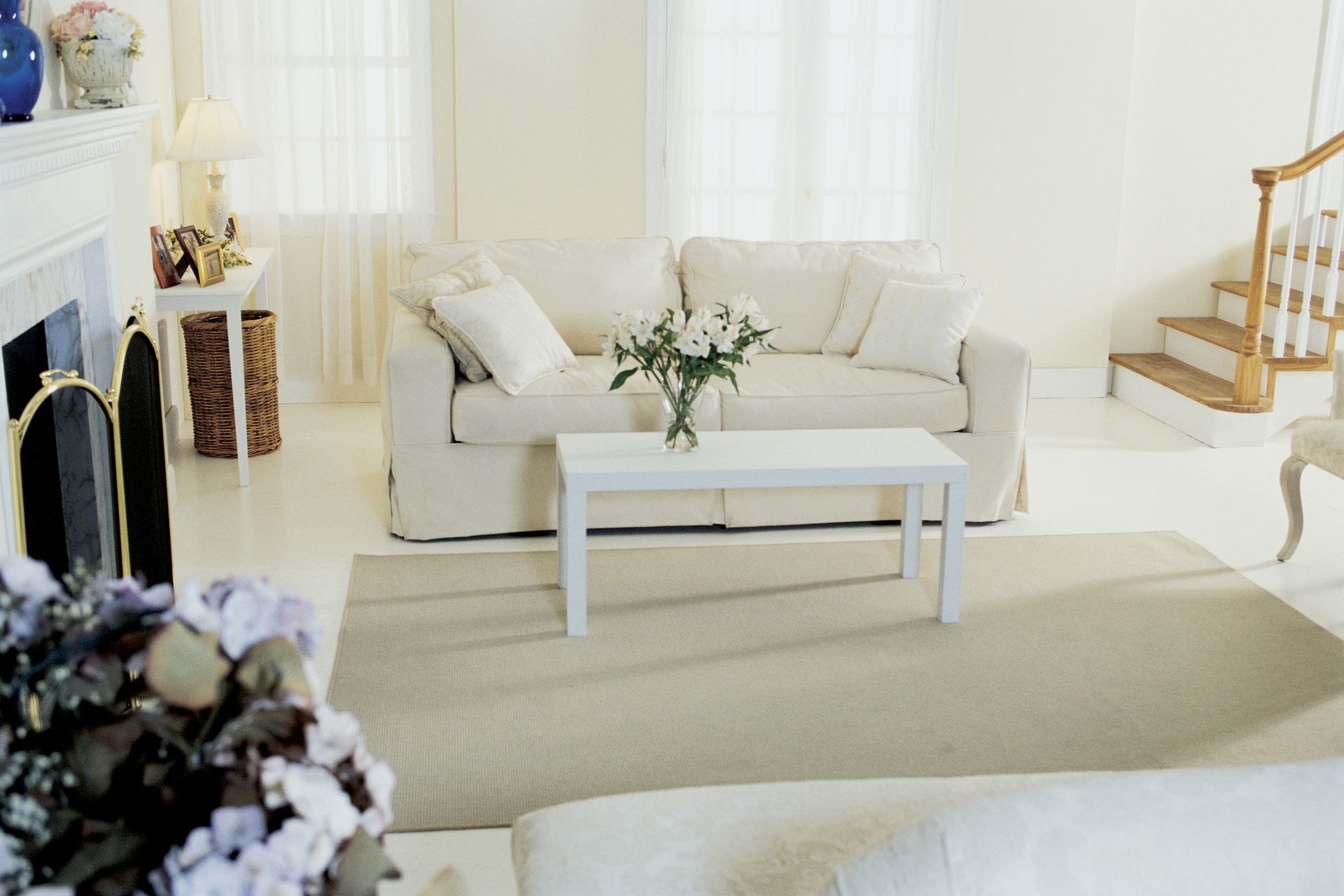 Bright living room with a cream sofa, white coffee table, and large windows with sheer curtains