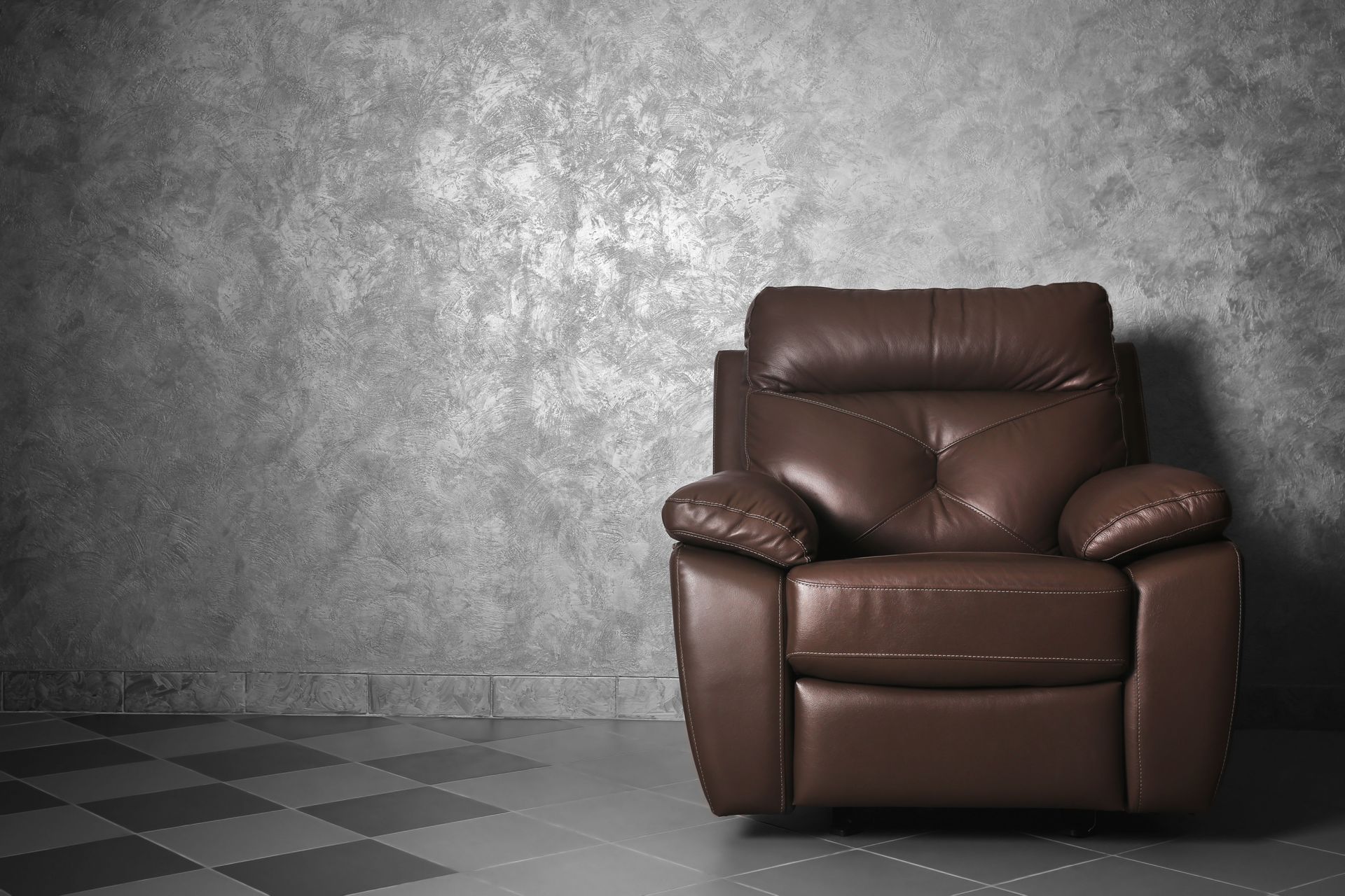 Brown leather armchair against a textured gray wall and checkered floor