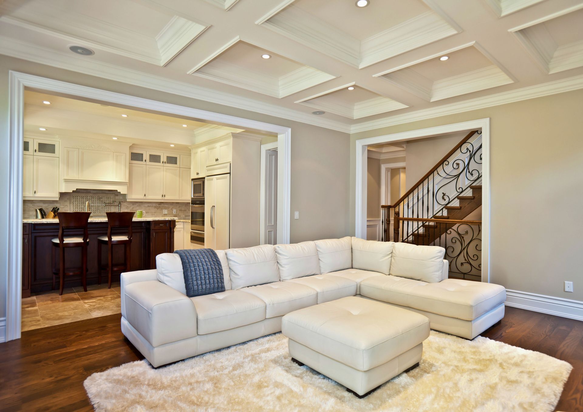 Modern living room with white sectional sofa, cream rug, and open kitchen in the background