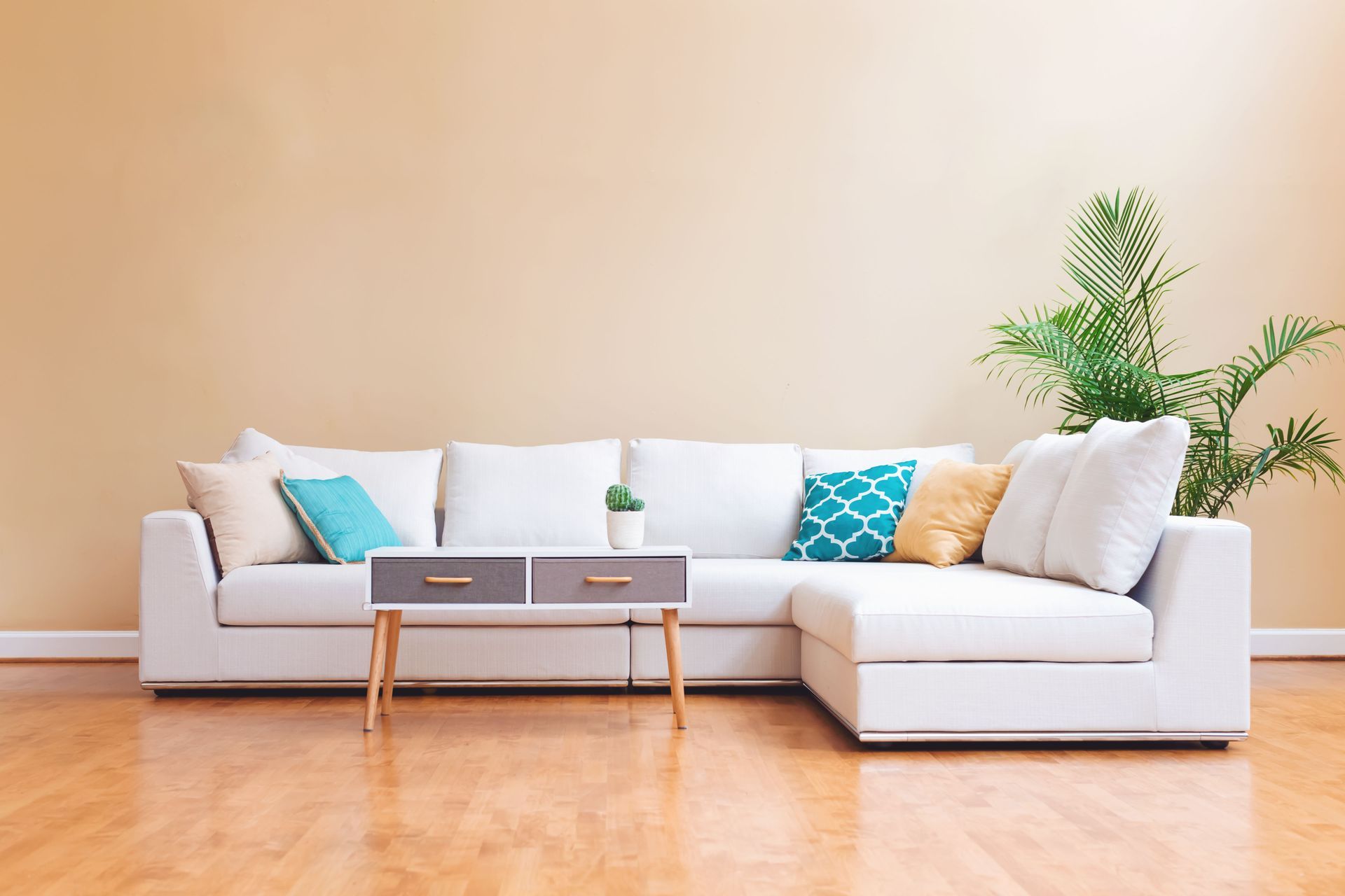 Modern living room with white sectional sofa, teal pillows, coffee table, and potted plant on a wood floor
