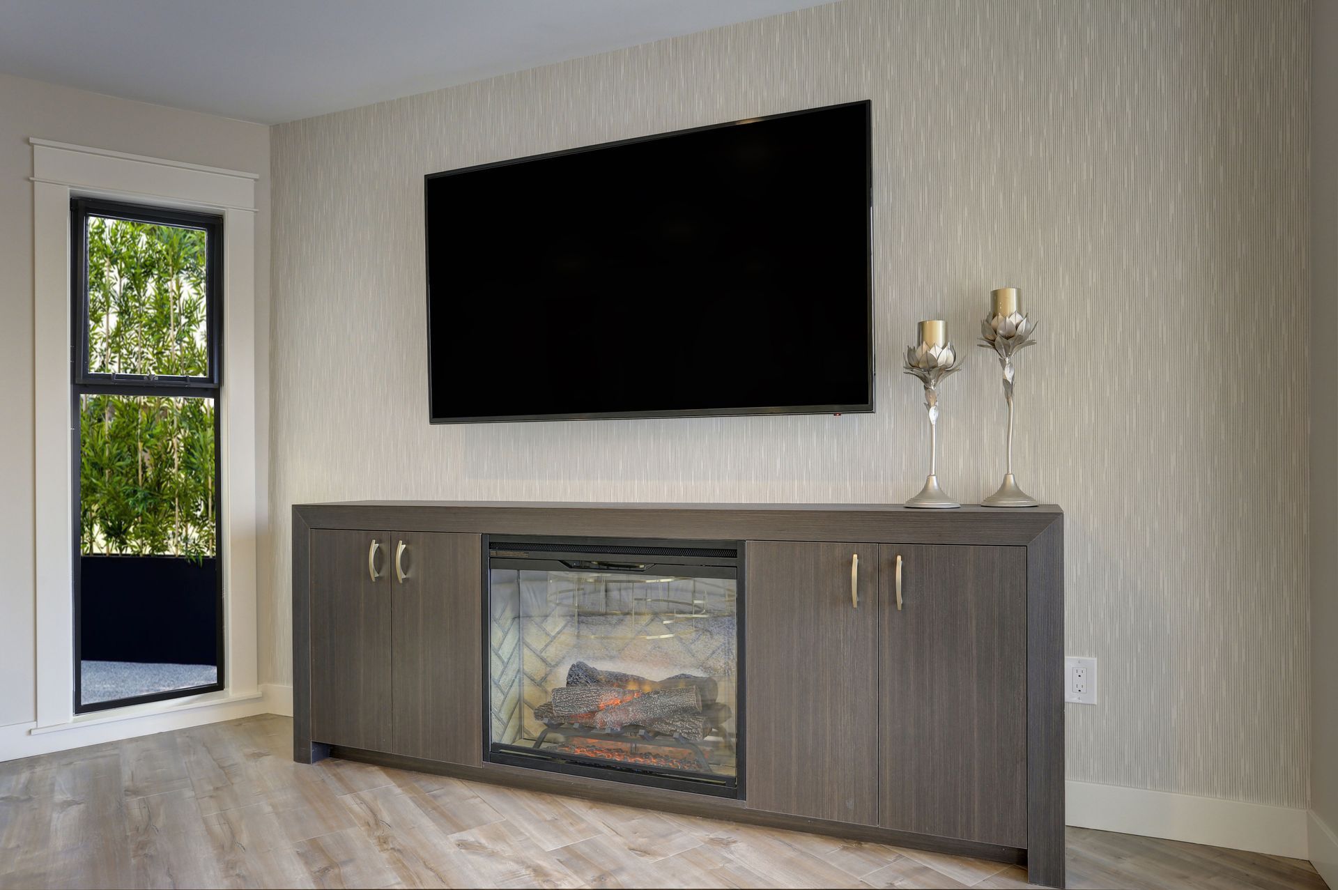 Modern living room with wall-mounted TV and gray fireplace console below, beside a window and floor lamp.