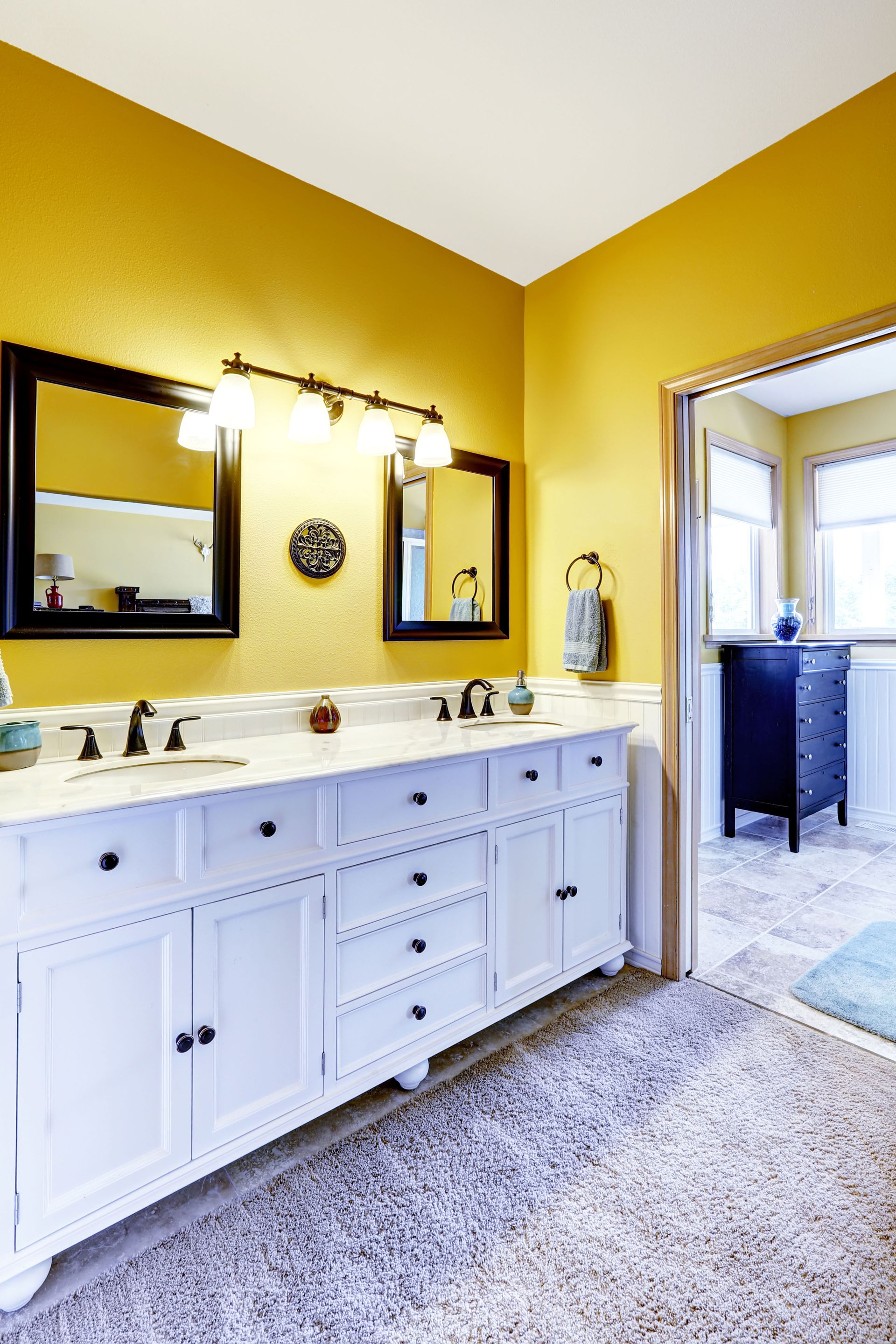 Yellow bathroom with white double vanity, mirrors, and gray rug by a doorway