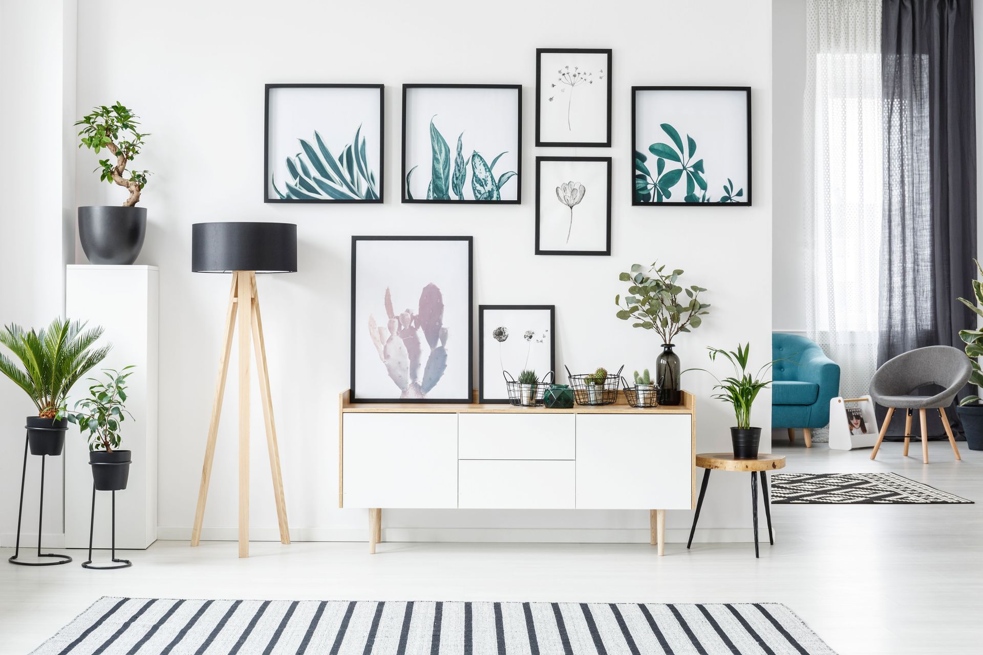 Bright minimalist living room with framed wall art, plants, a floor lamp, and a white sideboard.