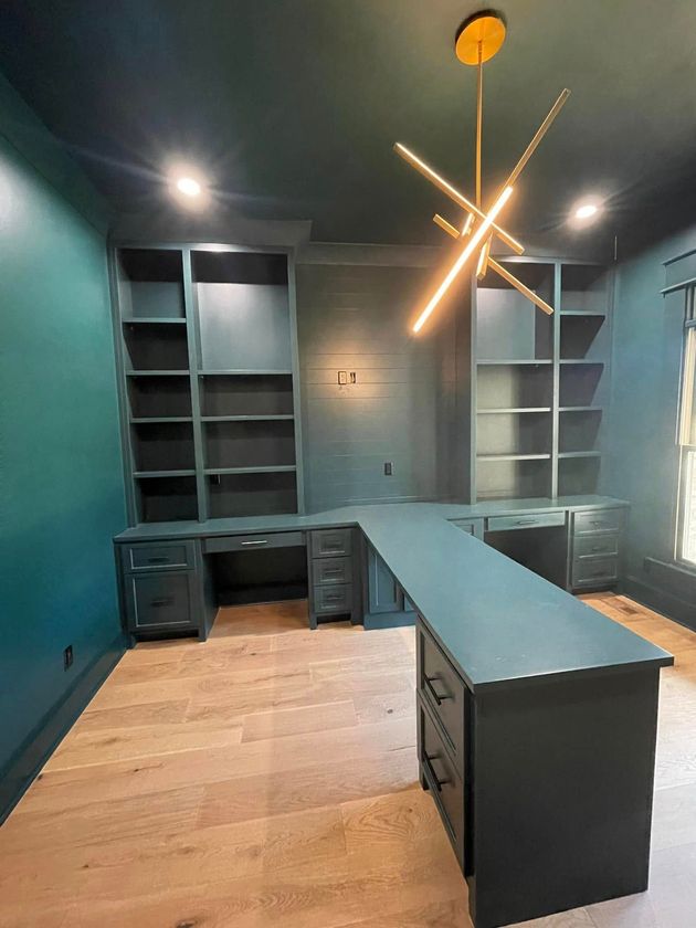 Modern office with teal walls, built-in shelves, dark desks, wood floor, and a starburst ceiling light.