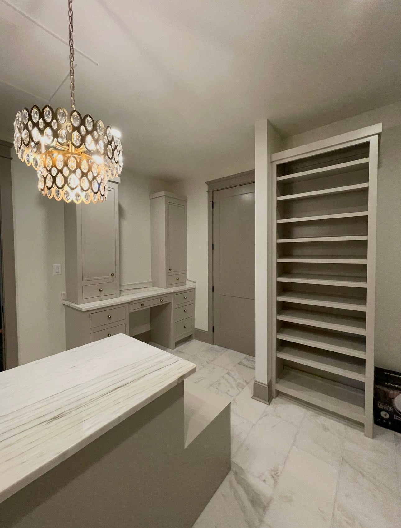 Elegant white closet/dressing room with built-in shelves, vanity, marble floor, and hanging chandelier