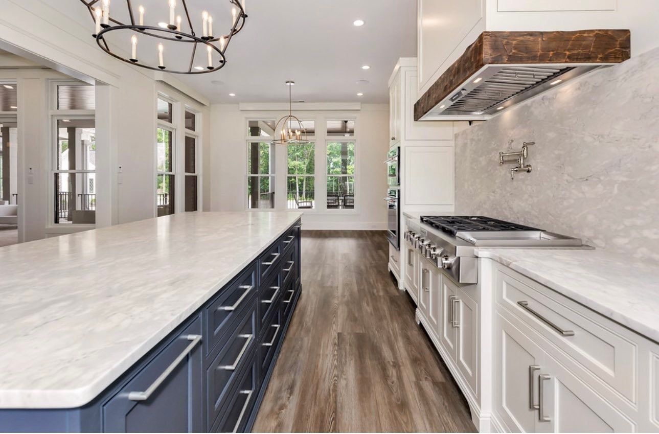 Bright modern kitchen with large white island, marble countertops, dark cabinets, and wood floors