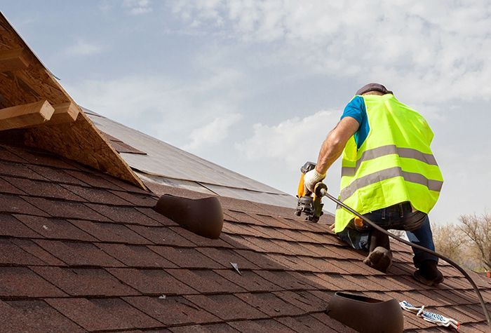 A man in a yellow vest is working on a roof.