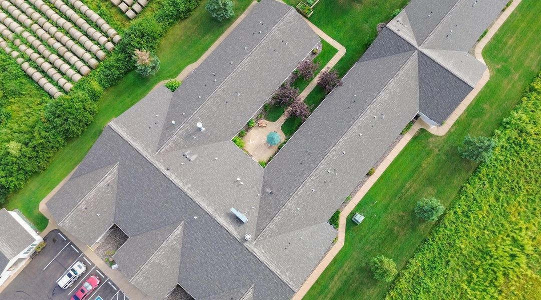 An aerial view of a large building with a lot of roofs surrounded by grass and trees.
