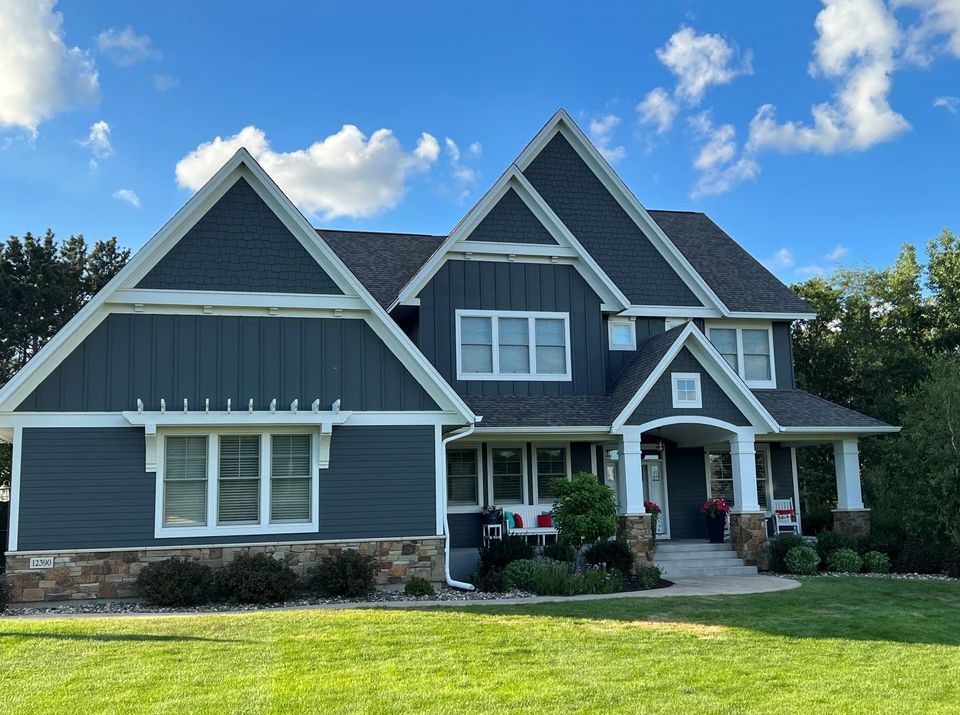 A large house with a blue siding and white trim is sitting on top of a lush green lawn.