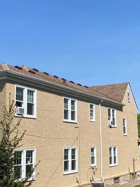 A large tan building with a brown roof and white windows.