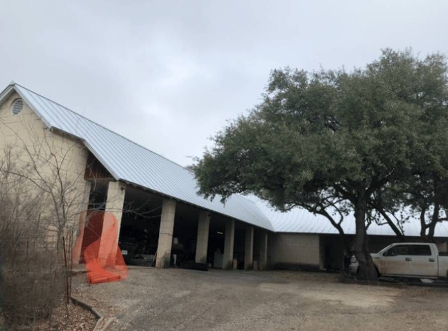 A white truck is parked in front of a large building with a metal roof