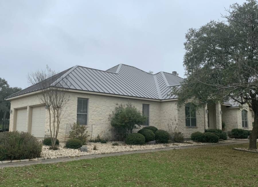 A white house with a metal roof is sitting on top of a lush green field