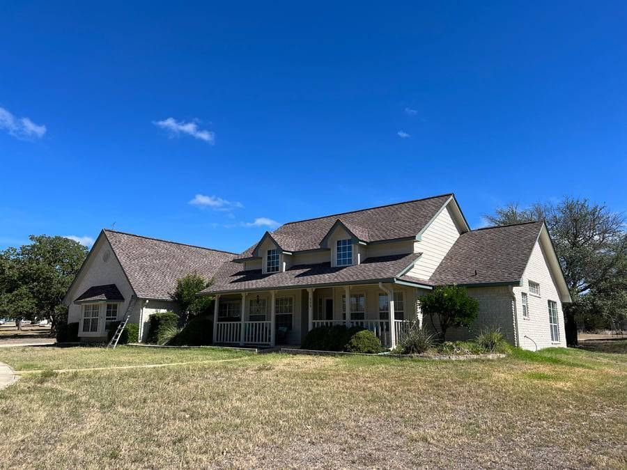 A large white house with a gray roof is sitting on top of a lush green field