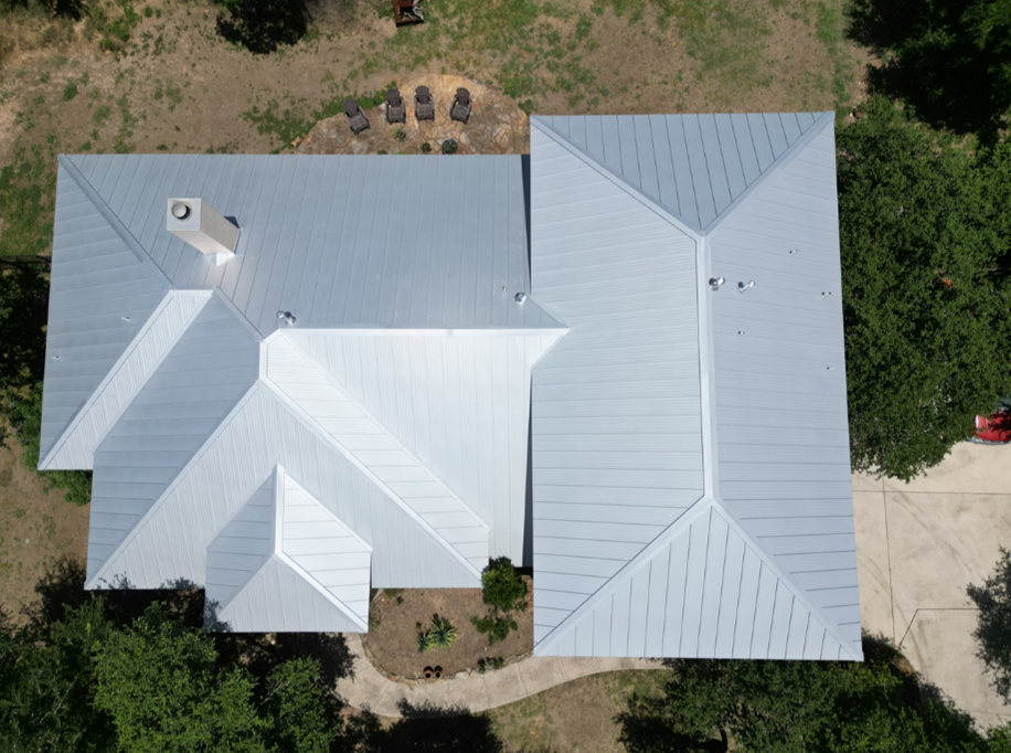 An aerial view of a house with a metal roof surrounded by trees