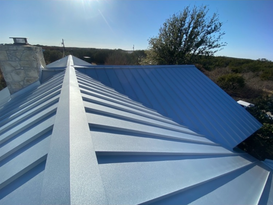 A blue metal roof with a chimney and trees in the background