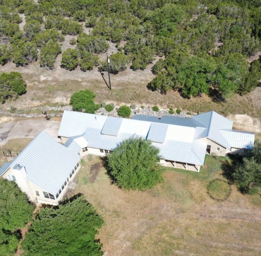An aerial view of a house with metal roof surrounded by trees and grass