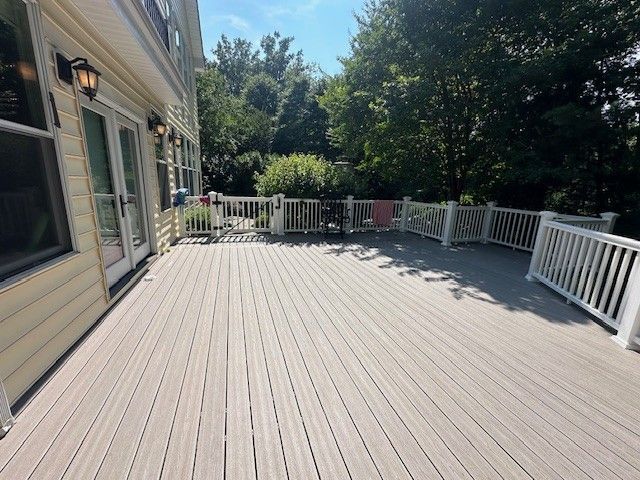 A nice-looking large deck with a white railing in front of a house.