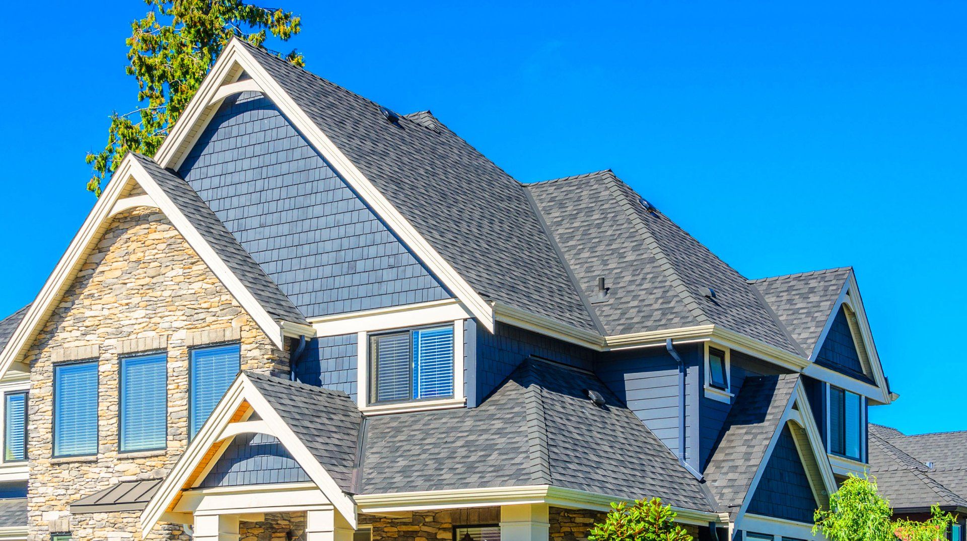 Learn More About Roofing A large house with a gray roof and a blue sky in the background.