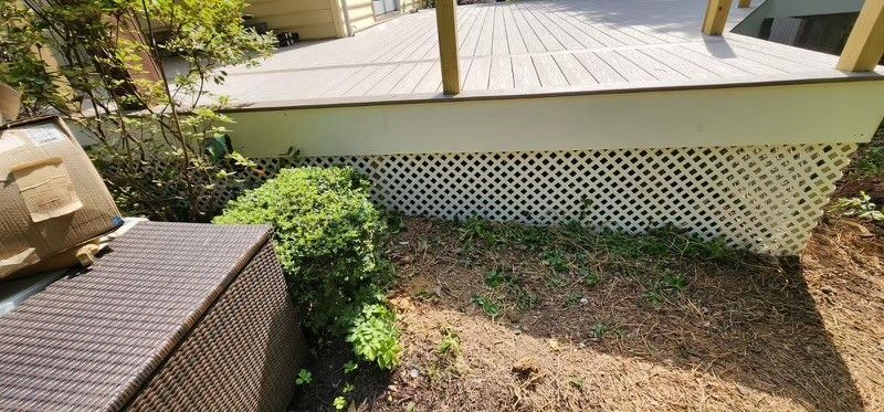 A wicker bench is sitting in the dirt next to a deck.