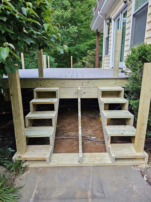 A wooden deck with stairs leading up to it and a house in the background.