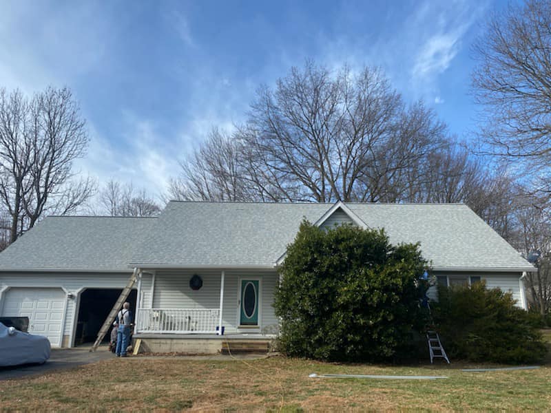 A man is standing in front of a white house with a gray roof.