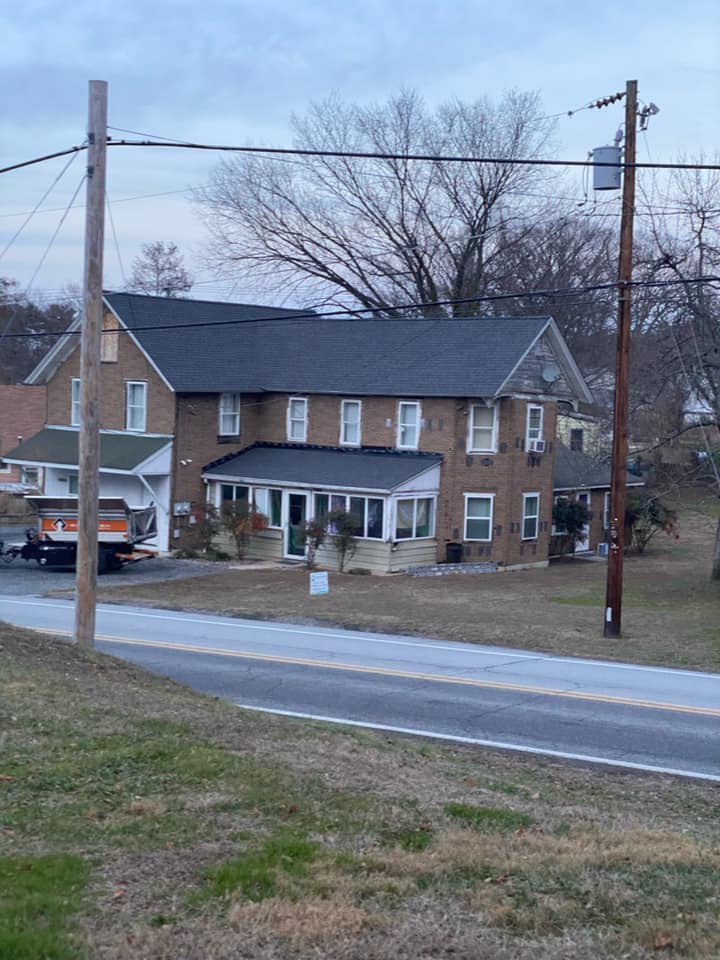 A large brick house with a black roof is sitting next to a road.